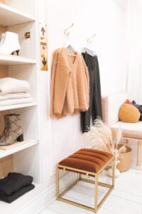 A wardrobe with clothes on shelves and some sweaters hung up in colours of ochres and ambers