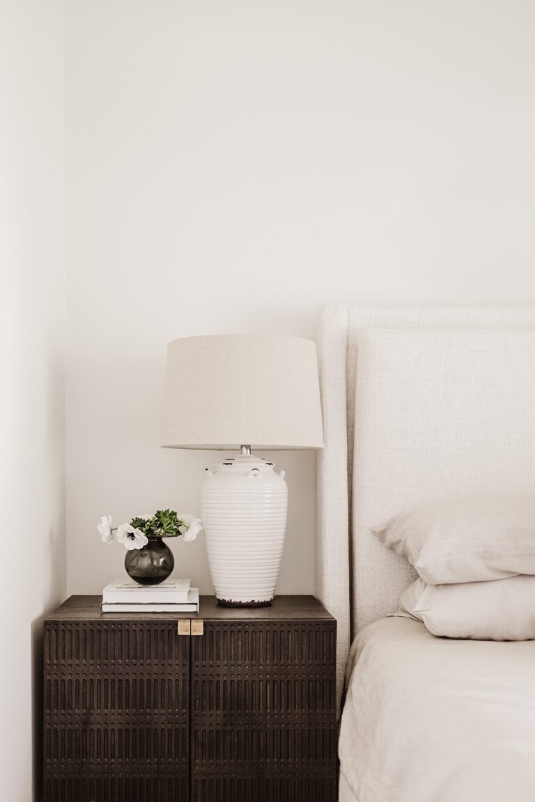 A bedside table with a lamp and small vase of anemones