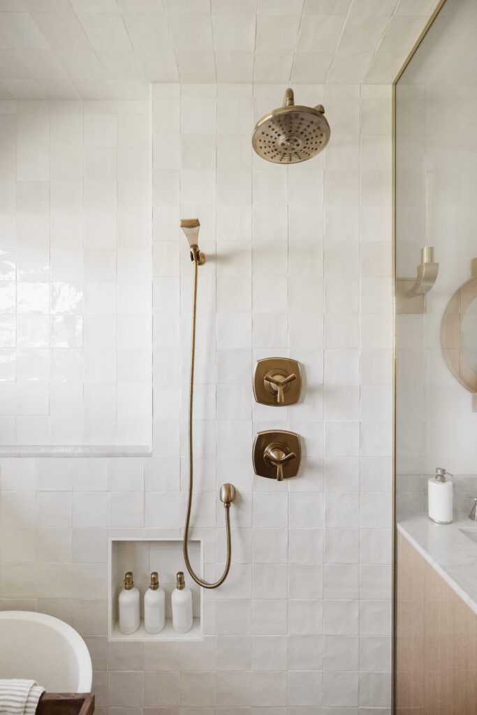 A minimalist shower space with white tiles and brass fittings