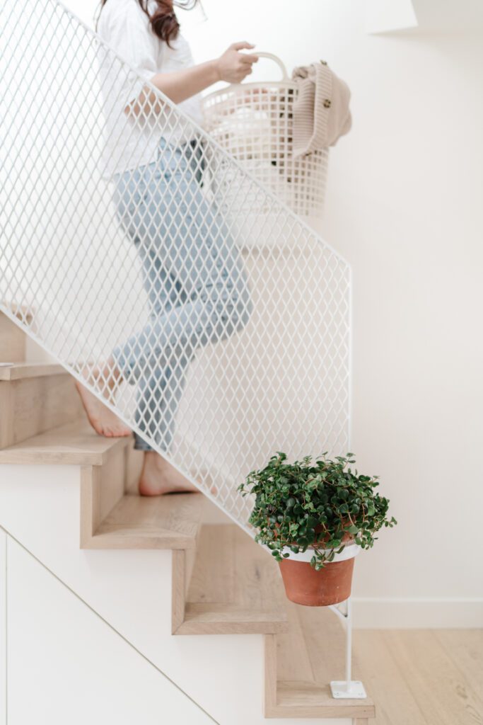 A woman in jeans walking downstairs with a laundry basket