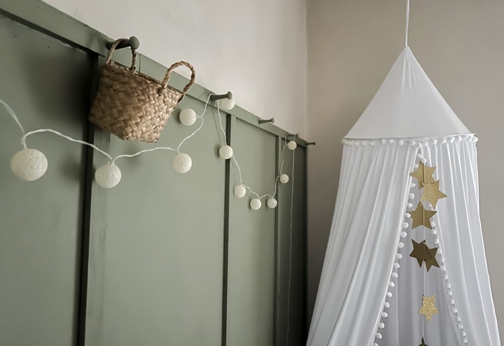 Close up of a shaker style panelled wall with pegs and small wicker baskets - walls are Farrow and Ball Lichen