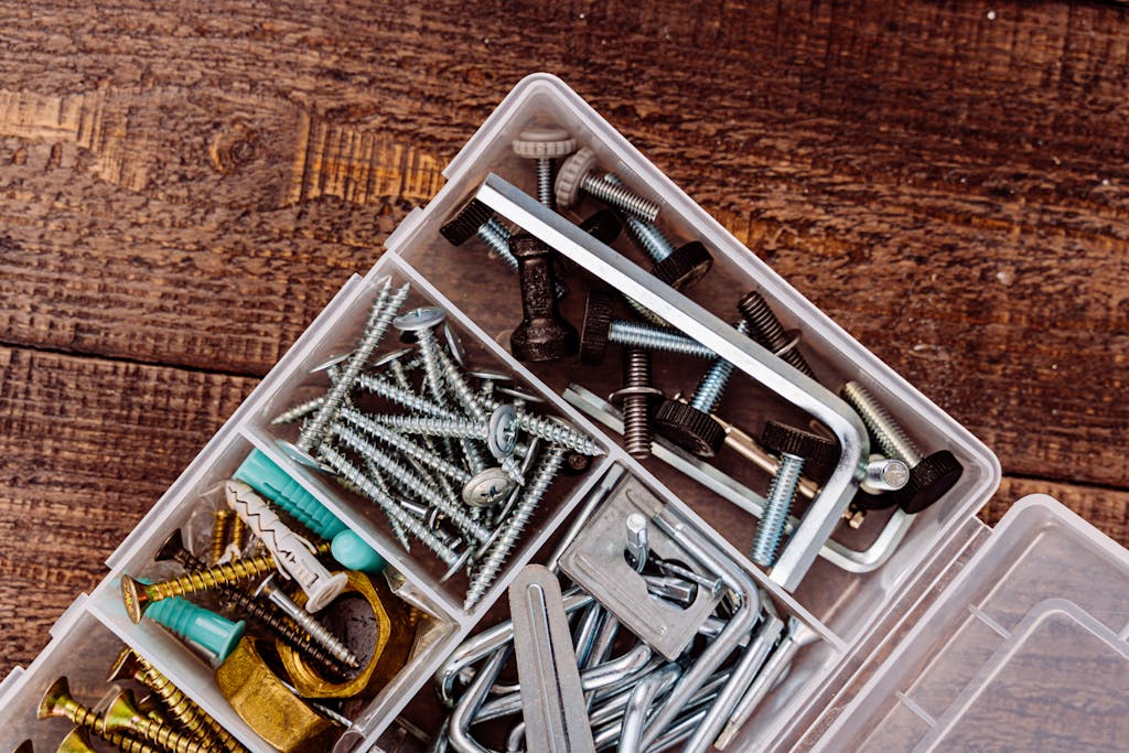 Top view of assorted screws and bolts in a plastic organizer on a wooden surface.