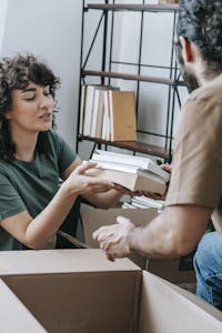 A couple happily packing books into boxes at home, preparing for a move.
