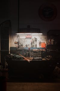 A moody, dimly lit workshop with neatly arranged tools and equipment, evoking a sense of craft and diligence.