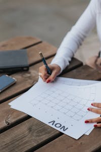 A woman writes on a November calendar outdoors, planning and scheduling her month.