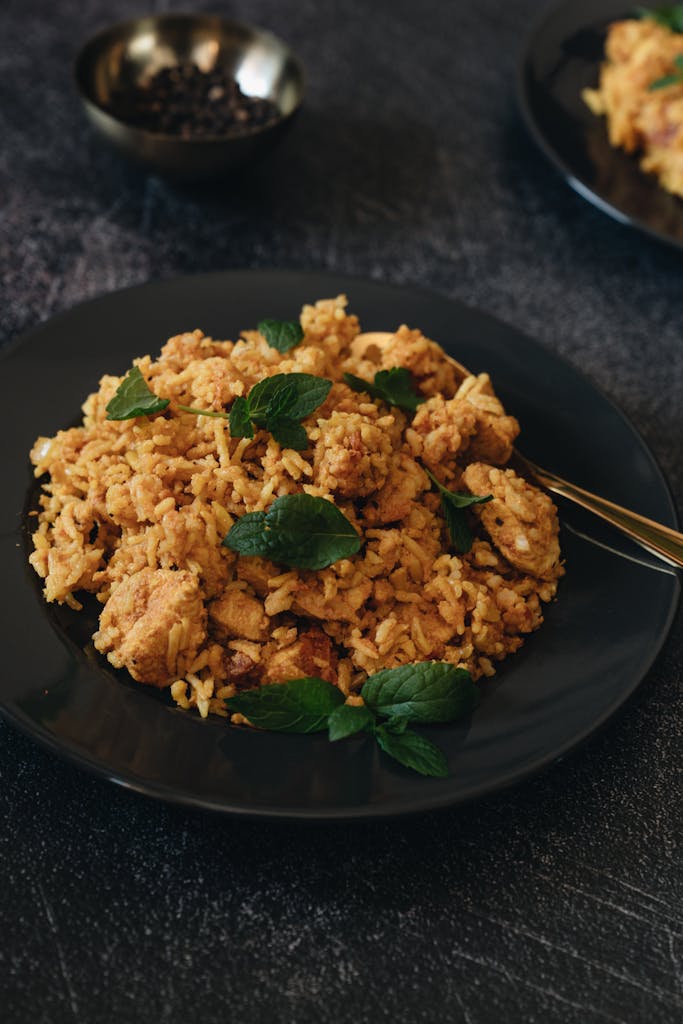 Appetizing chicken biryani garnished with mint on a black plate, perfect for dinner.