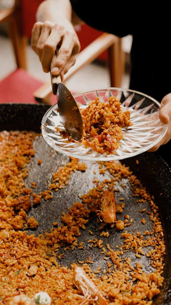 Close-up of a chef serving traditional Spanish paella with shrimp, showcasing culinary skills.