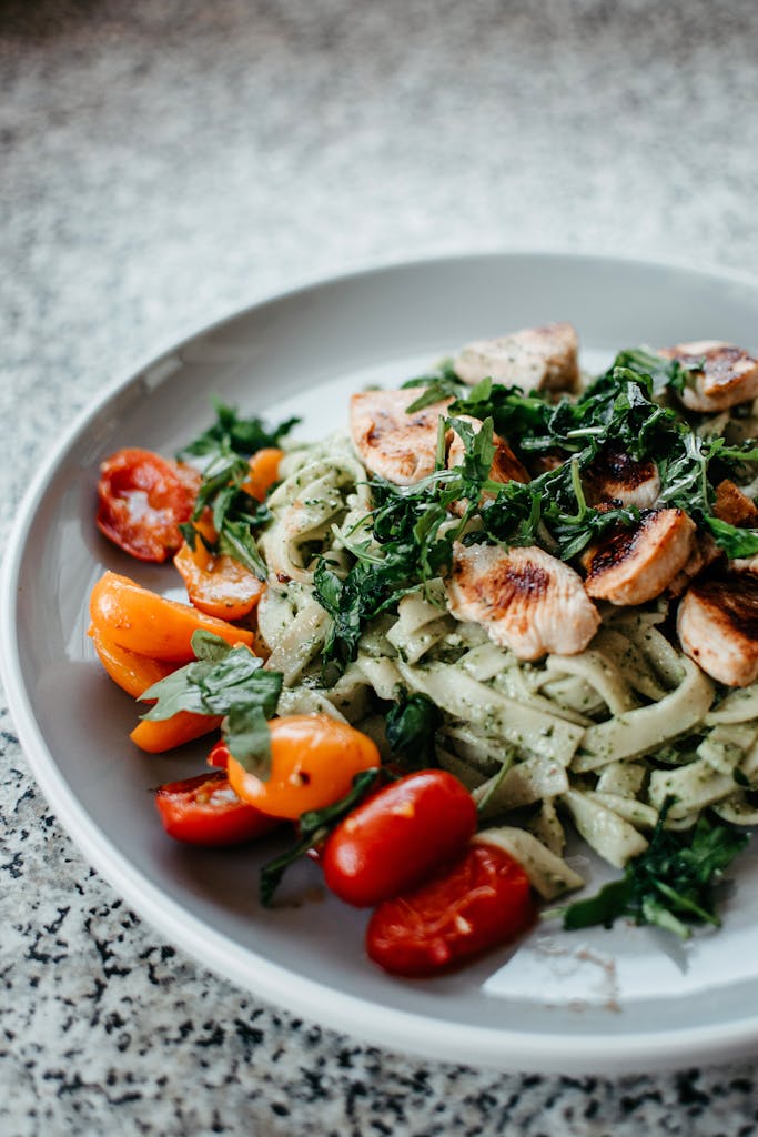 Close-up of a chicken pasta dish with cherry tomatoes and herbs on a gray plate.