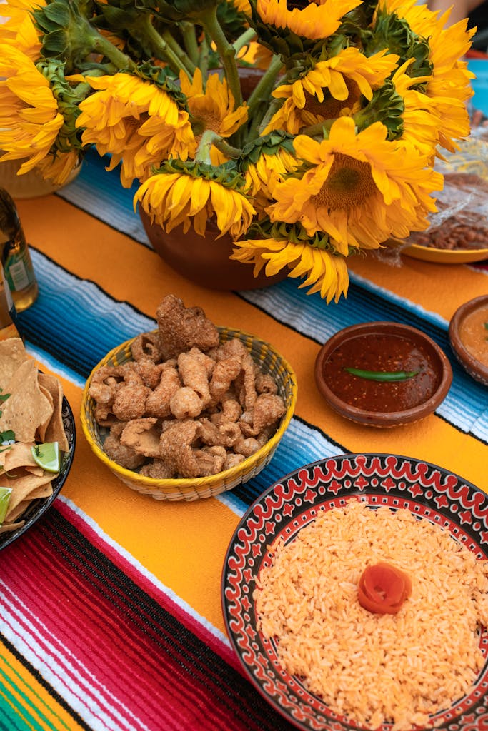 Colorful Mexican meal with rice, pork rinds, and sunflowers on a festive table setting.