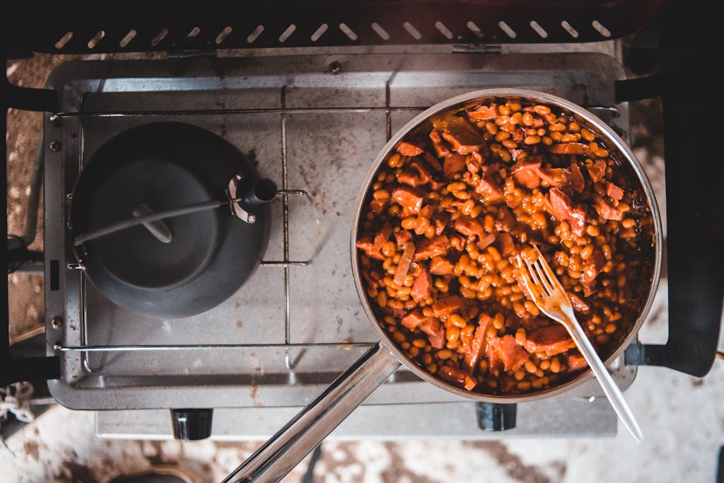Delicious baked beans and sausage simmering on a stove in a stainless steel pan.