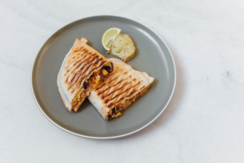 Delicious grilled quesadilla with corn, beans, and cheese on a plate, served with lemon slice.