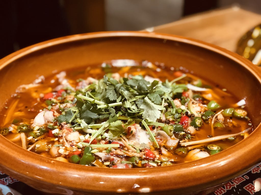 Delicious spicy soup with herbs in a clay pot, showcasing vibrant Asian cuisine.