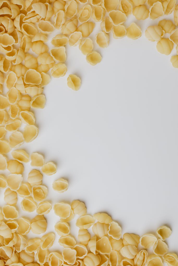 Overhead view of uncooked pasta shells scattered on a white surface.