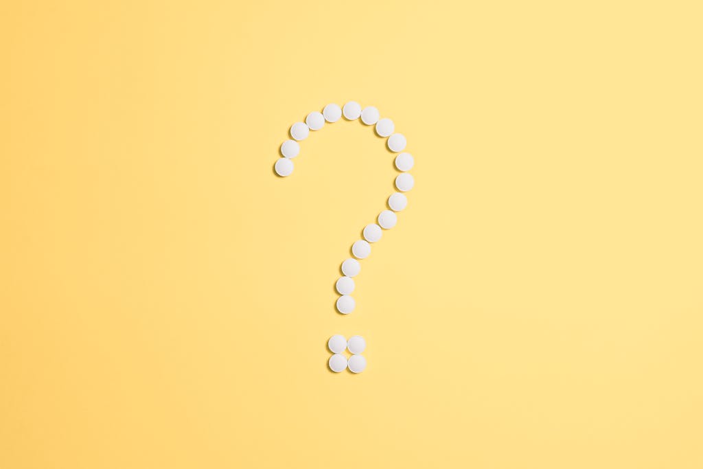 White pills arranged into a question mark shape on a vibrant yellow background.