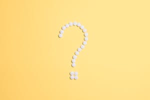 White pills arranged into a question mark shape on a vibrant yellow background.