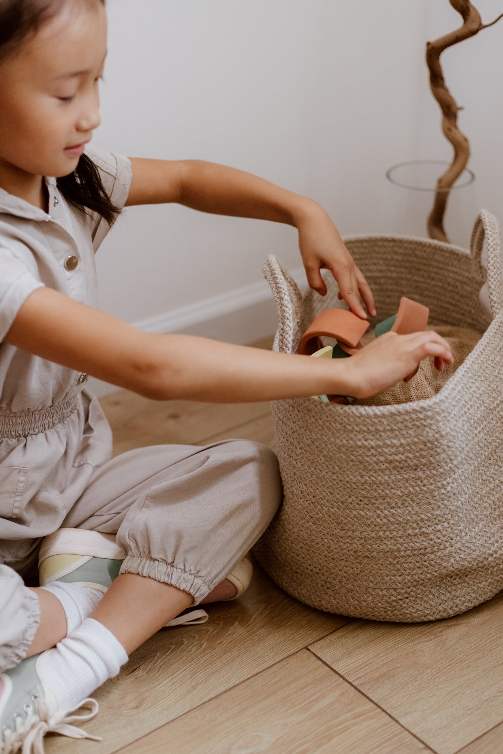 Young girl organizing toy blocks in a woven basket in a cozy indoor space.