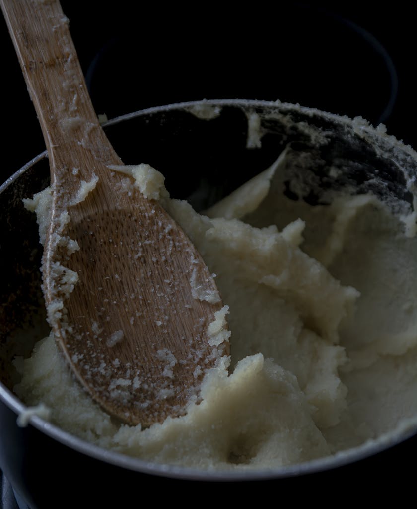 A close-up of creamy mashed potatoes in a pot with a wooden spoon, perfect for food enthusiasts.