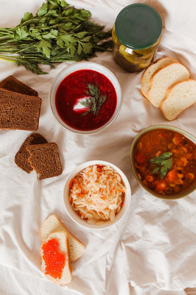 A top view photo of an assortment of soups, bread, and fresh vegetables on a white background.