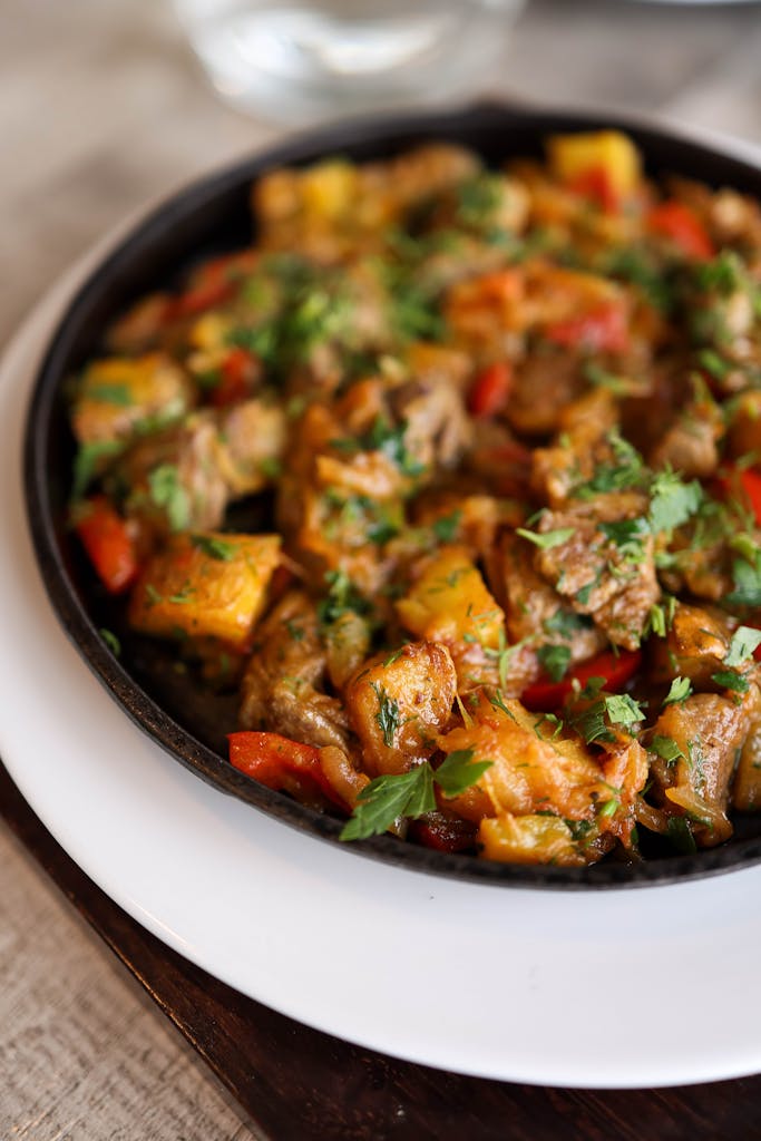 Close-up of a vibrant bell pepper and meat skillet, garnished with fresh herbs.