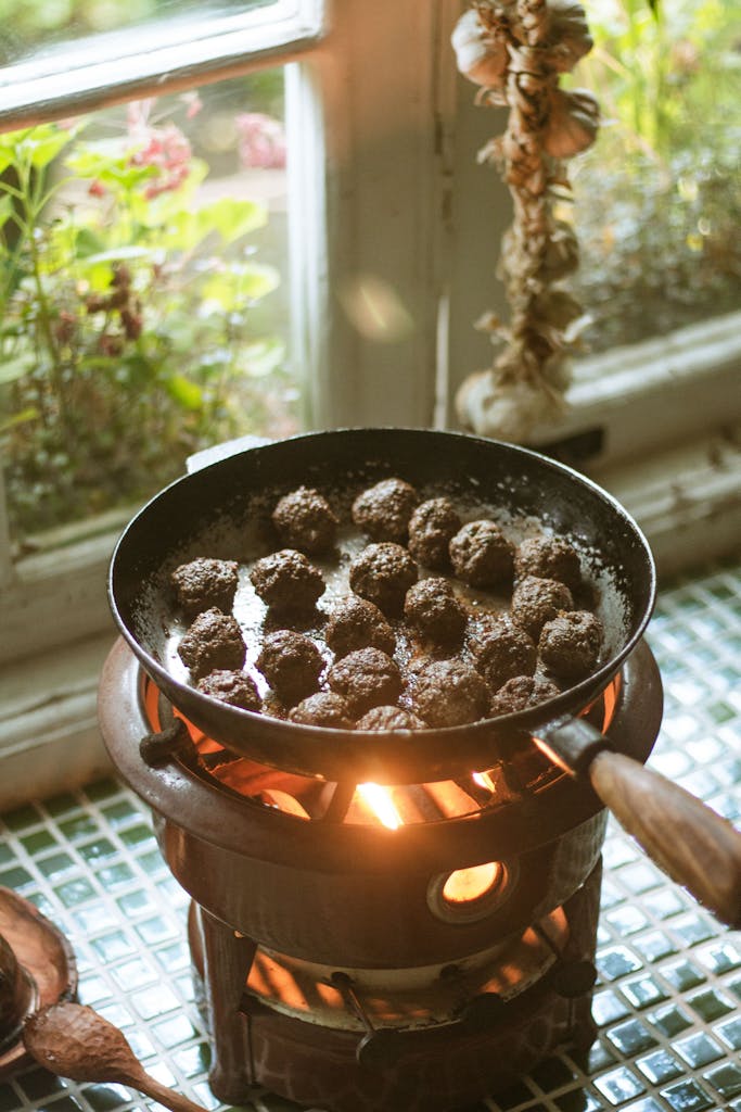Rustic indoor cooking scene with sizzling meatballs on a vintage stove.