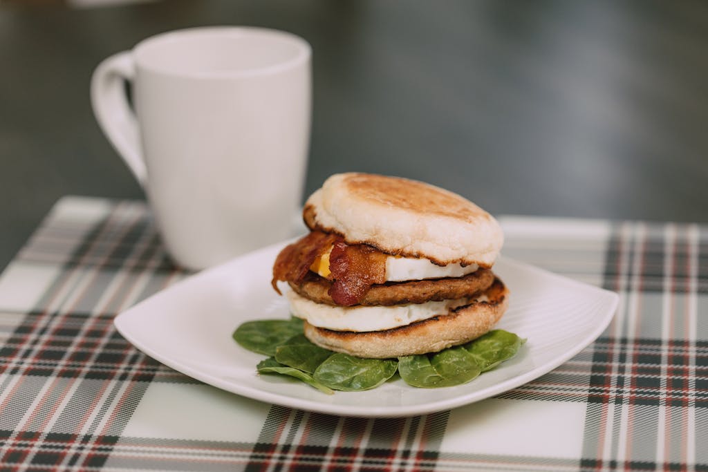 Tasty breakfast sandwich with bacon and spinach, served on a plaid tablecloth.