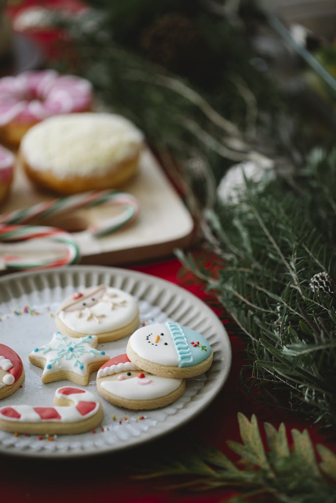 High angle of traditional Christmas gingerbread biscuits with colourful icing on plate on served table with desserts decorated with spruce twigs
