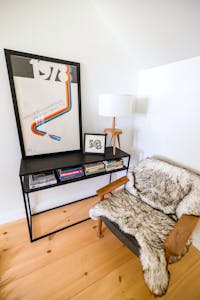 Inviting reading corner featuring an armchair, fur throw, books, and retro art in a modern Lake Placid home.
