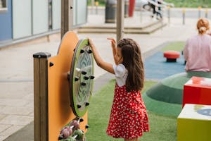 Side view of little girl playing with toy on playground in casual outfit in daytime on street